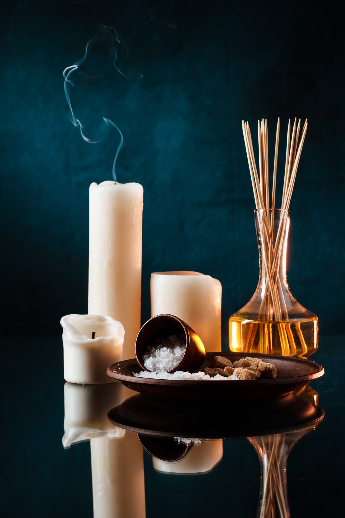Duftdiffuser mit Stäbchen, weiße Kerzen und Meersalz in einer Wellness-Atmosphäre.