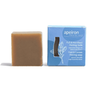 Ein Stück Apeiron Fuß- & Hornhaut Peeling-Seife neben der blauen Verpackung.