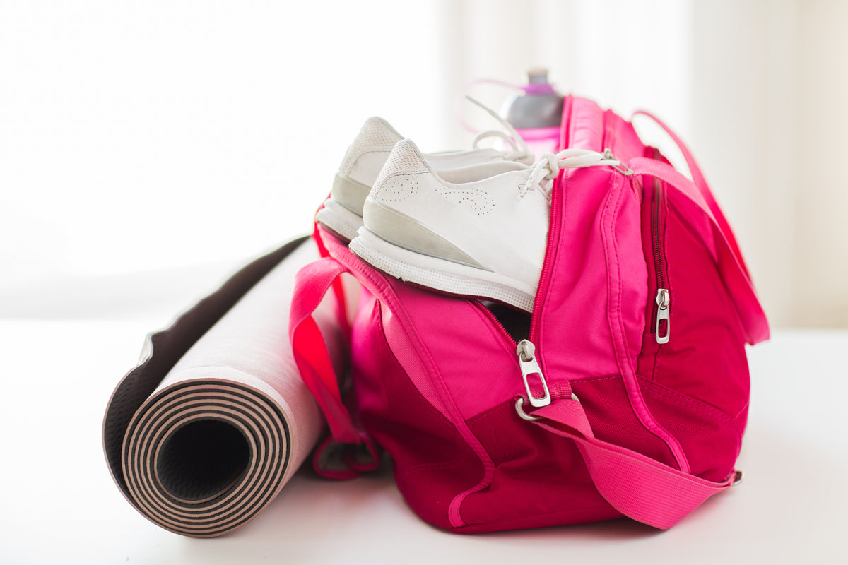 Rosa Sporttas mit weißen Turnschuhen und zusammengerollter Yogamatte für Fitness und Yoga.