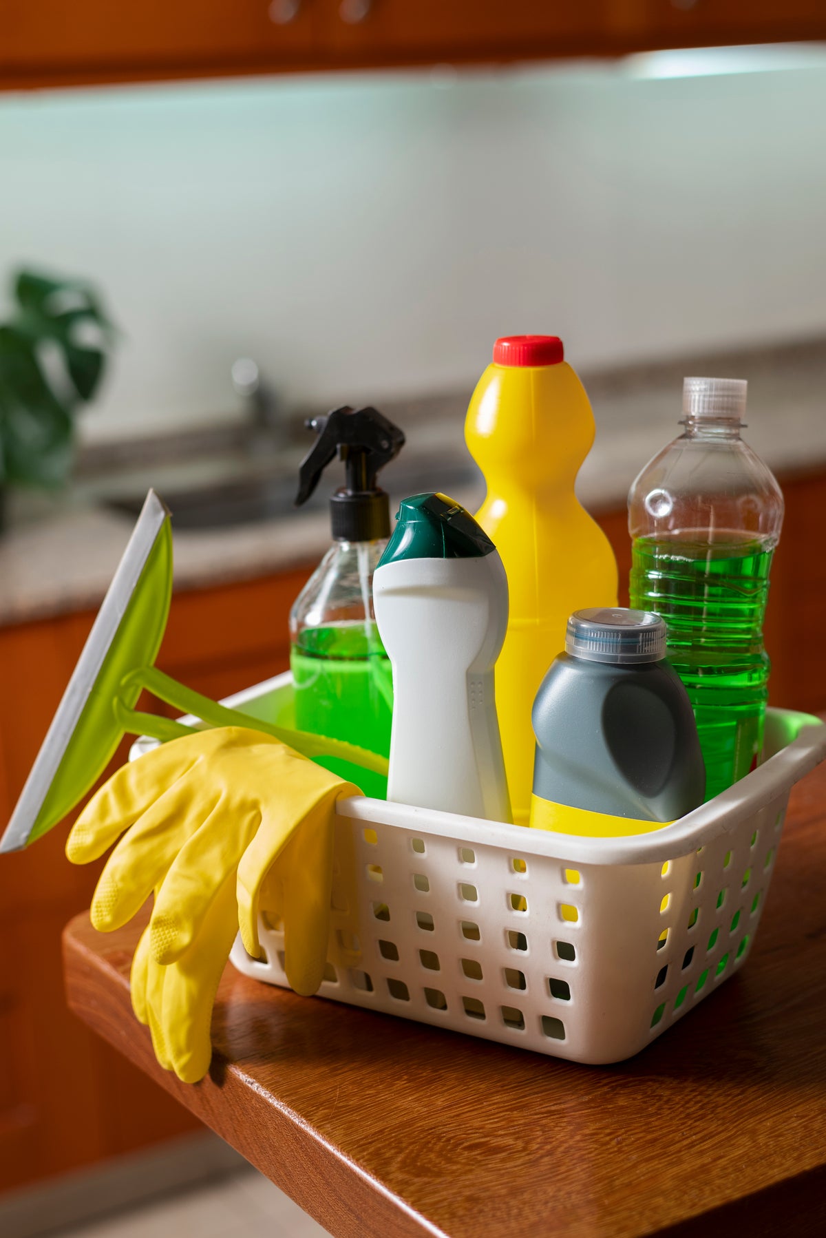 Reinigungsmittel und gelbe Gummihandschuhe in einem weißen Korb in der Küche.