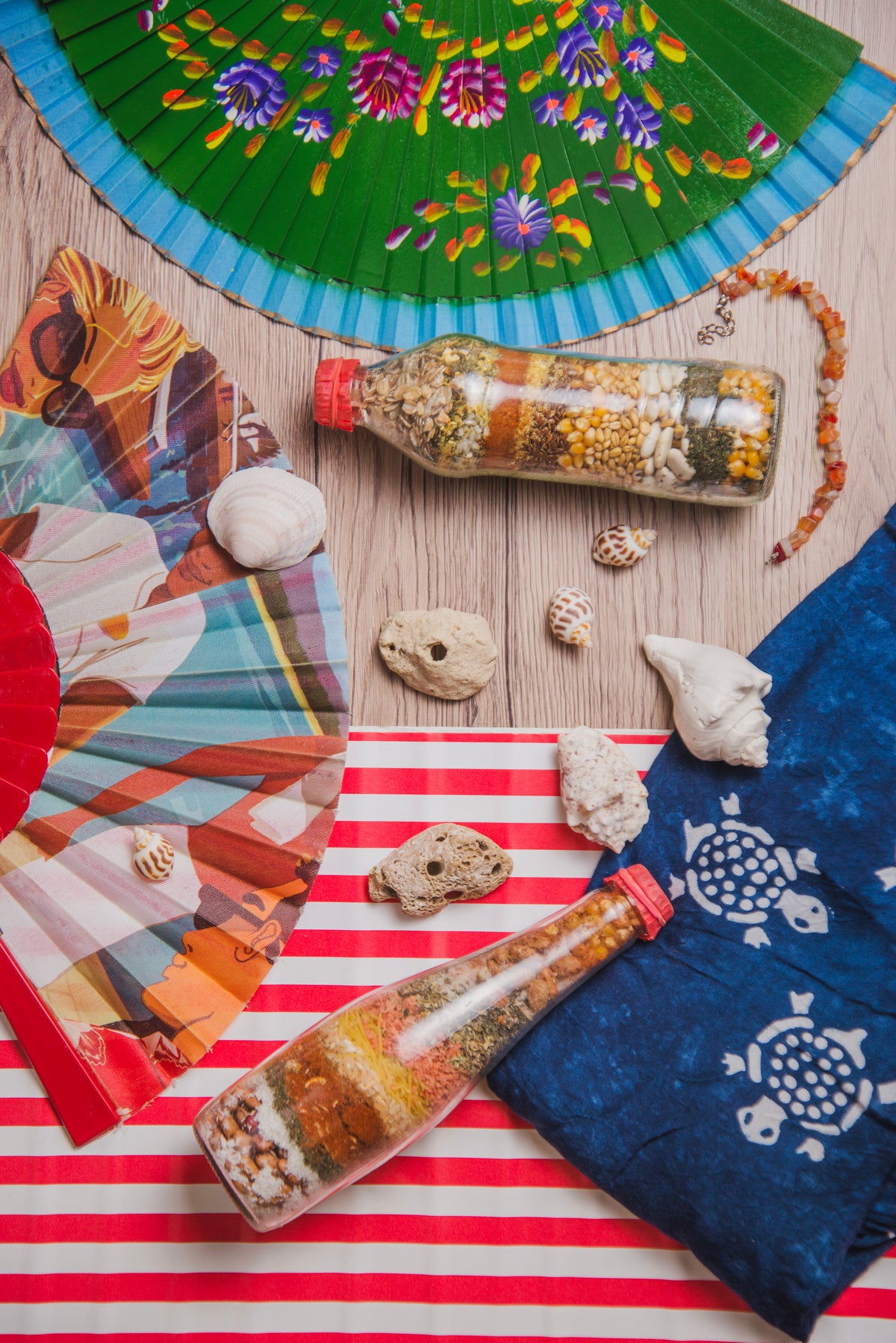 Sommerliche Dekoration mit Fächern, Muscheln und Gläsern voller Gewürze auf Holz.