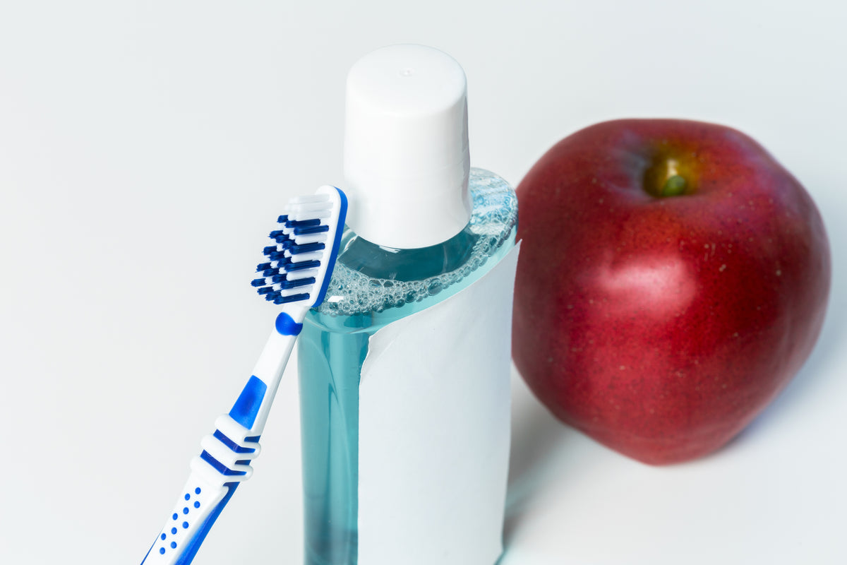 Zahnbürste, blau-weiße Mundspülung und ein roter Apfel auf weißem Hintergrund.