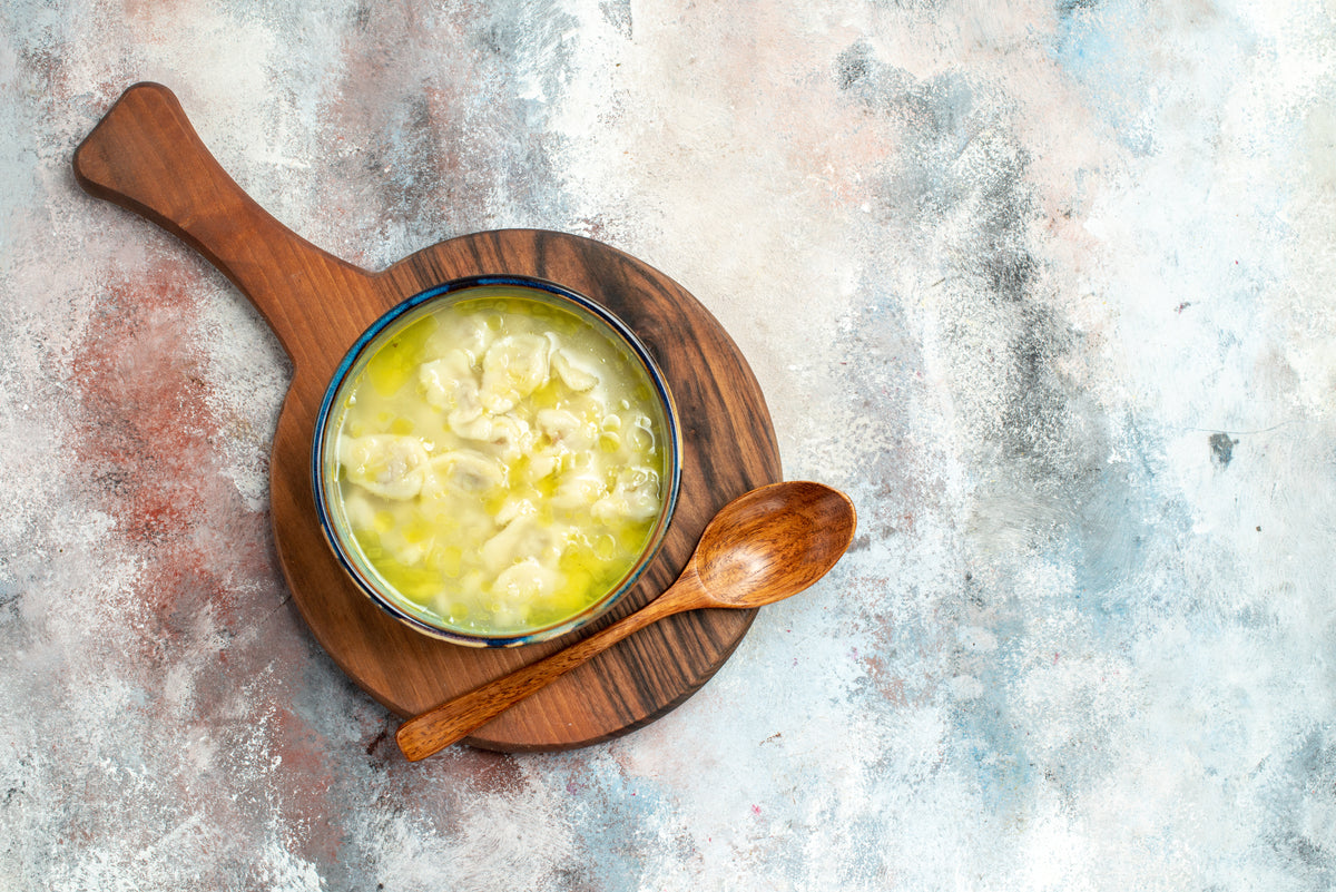 Warme Suppe mit Teigtaschen in einer Schüssel auf einem Holzbrett.