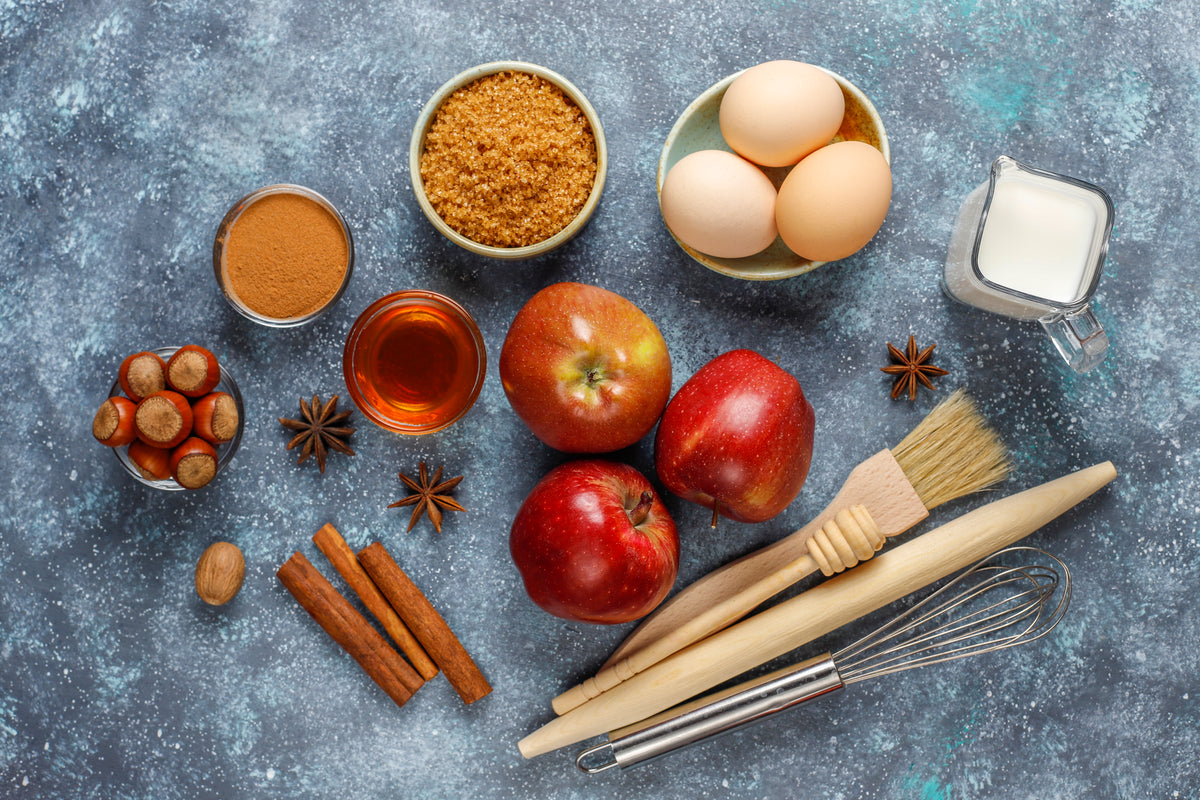 Frische Äpfel, Eier, Zucker und Gewürze für gesunde Backzutaten auf grauem Hintergrund.