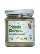 Ein klarer glasbehälter mit braun-grünem triphala churna bio pulver aus terminalia chebula und emblica officinalis