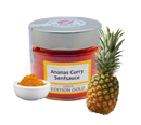 Ein glas mit roter ananas curry senfsauce von ulrika’s manufaktur mild curry paste neben ananas und gewürzschale