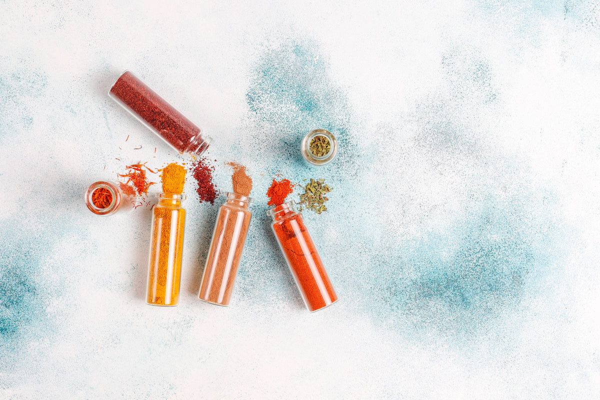 Verschiedene Bio-Gewürze in kleinen Glasfläschchen auf hellem Untergrund.