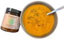 Eine lebendige orangefarbene suppe in grauer keramikschale mit vata spice blend als wärmende hydrierende verdauungs-churna von paavani ayurveda