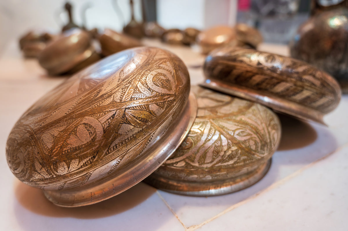 Handgefertigte, verzierte Metallschalen mit traditionellen Mustern auf hellem Untergrund.
