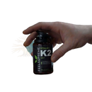 Eine dunkle bernsteinfarbene glasflasche mit vitamink2 mk7 bioaktive form supplementen von mana shop mit schwarzem verschluss und grünem blattetikett