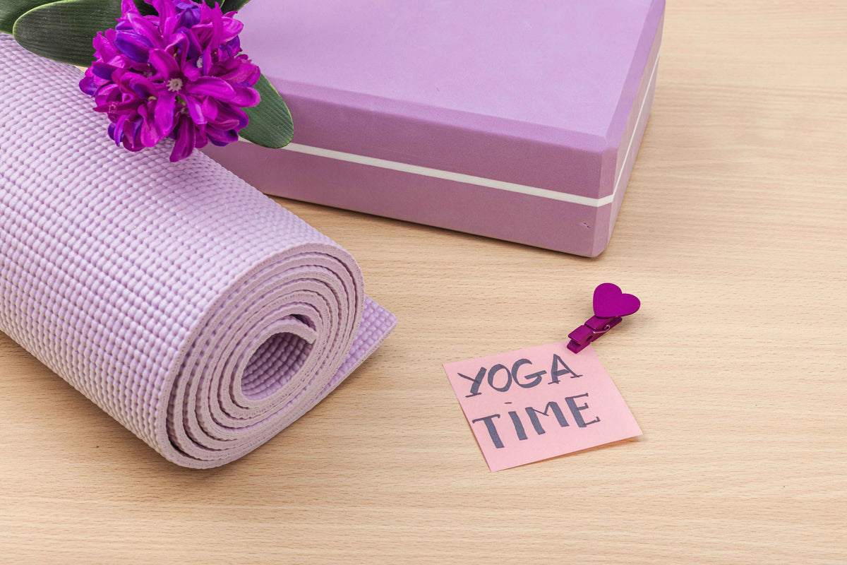Lila Yogamatte, Geschenkbox und Zettel mit der Aufschrift Yoga Time auf hellem Holz.