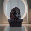 Ein Zimmerbrunnen mit einer meditierenden Buddha-Statue und kaskadierenden beleuchteten Schalen vor einem runden Fenster.