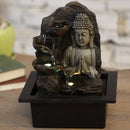 Ein Buddha-Zimmerbrunnen mit Wasser, das über drei beleuchtete Schalen auf einer Holzoberfläche kaskadiert.